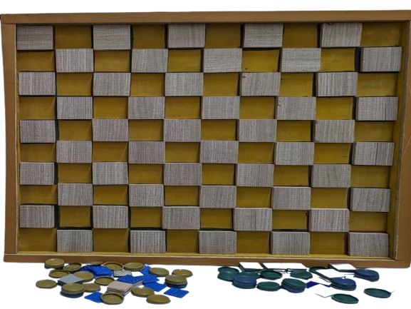 he image shows a checkerboard with a wooden frame. The board has alternating squares of yellow and a textured grayish-white color. In front of the board, there are several circular game pieces scattered on the surface. These pieces are in two colors: a light brownish-yellow and a dark greenish-blue. The arrangement suggests that this is a setup for a board game, possibly checkers or a similar game.